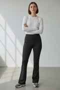 Donna indossa pantalone a zampa nero elasticizzato a vita alta con fondo flare. Abbinamento casual con maglia bianca e sneakers.