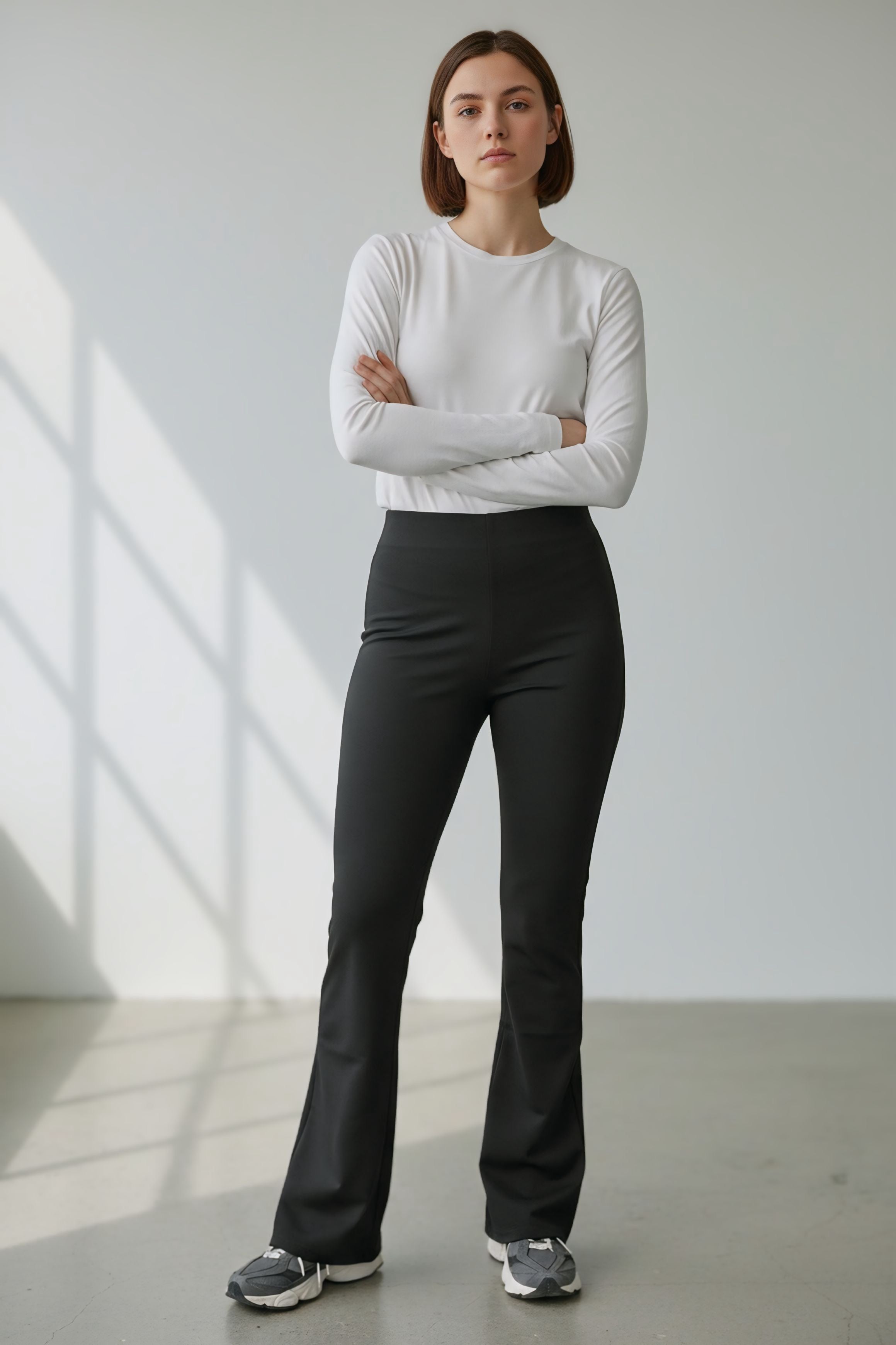 Donna indossa pantalone a zampa nero elasticizzato a vita alta con fondo flare. Abbinamento casual con maglia bianca e sneakers.